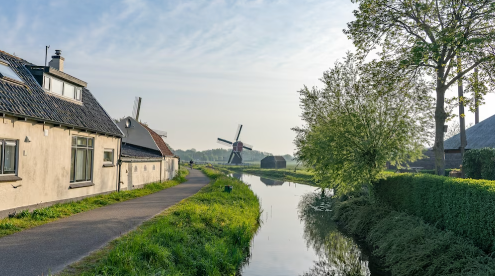 water canal at the side of a narrow road with a windmill on a field